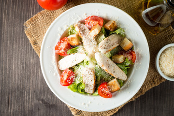 Fresh salad made of tomato, ruccola, chicken breast, eggs, arugula, crackers and spices. Caesar salad in a white, transparent bowl on wooden background