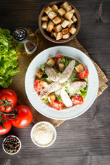 Fresh salad made of tomato, ruccola, chicken breast, eggs, arugula, crackers and spices. Caesar salad in a white, transparent bowl on wooden background