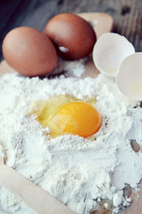 White flour with eggs, butter and wooden spoon on a cooking board