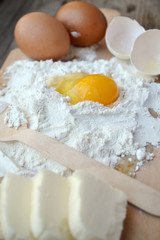White flour with eggs, butter and wooden spoon on a cooking board