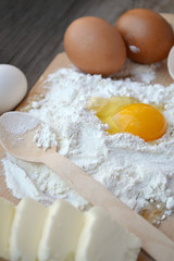 White flour with eggs, butter and wooden spoon on a cooking board