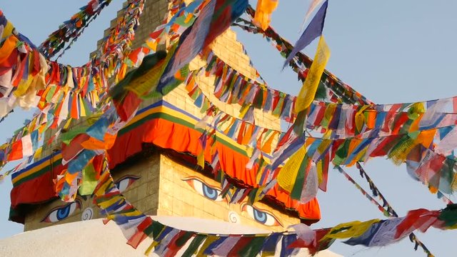 Colorful prayer flags flying in the wind at Boudhanath Stupa, Holy Pagoda, symbol of Nepal and Kathmandu with golgen Buddha's Eyes. Sunset ligth.
