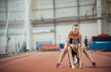 Two young women with blonde hair doing exercises and warming up together. A woman sits on the back of another woman