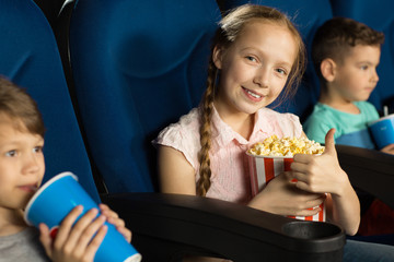 Cheerful young girl showing thumbs up at the cinema