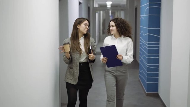 two young candid business woman walking trough the office, speaking and discuss something.