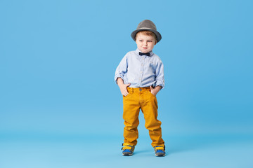 Portrait of happy joyful  little boy isolated on blue background. Toddler child in hat and fashionable suit smiling and have a fun. Copy space for text left side