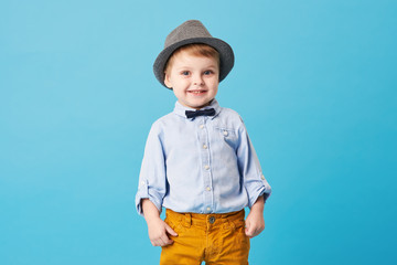 Portrait of happy joyful  little boy isolated on blue background. Toddler child in hat and fashionable suit smiling and have a fun  © oes