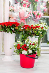 fresh flowers - red roses and white eustomas - in front of a floristry shop window, where elegant delicate bouquets stand in anticipation of a buyer