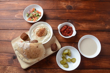 Falafel in pita bread with vegetable salad, harissa sauce, humus, tahini on wooden background. Traditional Israeli food. Middle eastern fast food concept
