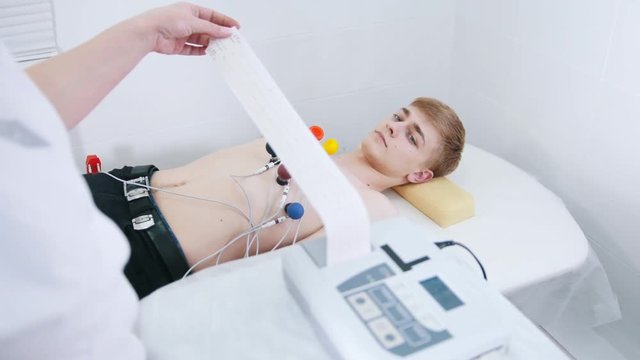 A medical clinic. A man receiving a ECG procedure. A results tape