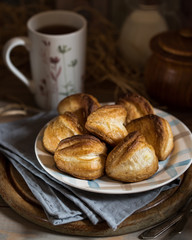 Greek cheese puffs on the old board, near vintage spoons, cup of tea, napkins. Puff pastry dumplings with feta cheese. Rustic style.