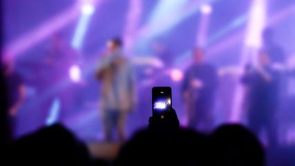 Person in audience holding cell phone in the air recording video of rock concert. Silhouette hand and blurry background