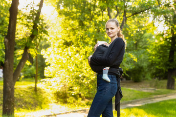 Young mother carrying a newborn sleepimg baby. Front wrap cross carry