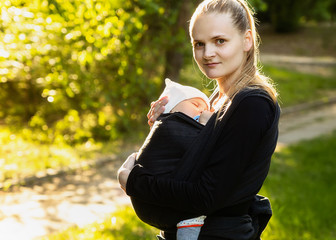 Young mother carrying a newborn sleepimg baby. Front wrap cross carry. Winding sling for carrying a child