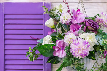 Fototapeta na wymiar Garden design and decor to decorate the exterior of the facade of the house. A bouquet of different colors of purple hanging in a pot on the wall by the window.