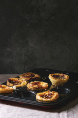 Traditional Portuguese egg tart dessert Pasteis Pastel de nata in black baking tray standing on linen table cloth near dark grey wall.