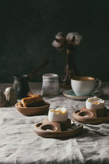 Breakfast with cup of coffee and soft boiled egg, served in wooden egg cup with salt, pepper and toasted bread, jug of cream and cotton flowers over linen tablecloth.