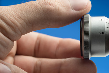 Male hand rotates the aluminum knob on a blue background. Side view.