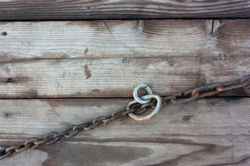 The metal chain lies on the old wet boards.	