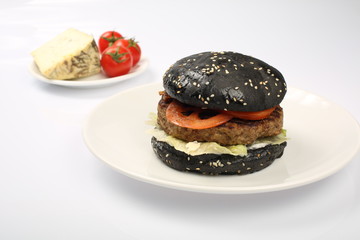 cheeseburger with black bread, beef cutlet, bacon, tomatoes and cheese slices, seasoned with sauce and green salad for a restaurant menu on a white isolated background