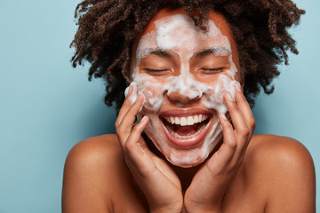 People, skin care and rejuvenation concept. Pleased dark skinned woman with soft skin, applies...
