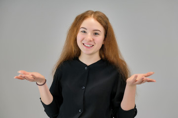 Concept portrait of a cute pretty teenager girl with red hair on a gray background smiling and talking.