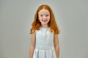 Concept portrait of a cute pretty child girl with red hair on a gray background smiling and talking