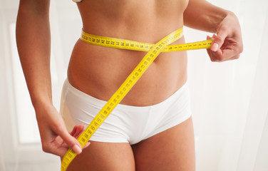 Slim young woman measuring her thin waist with a tape measure