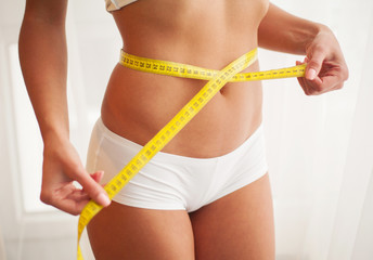 Slim young woman measuring her thin waist with a tape measure