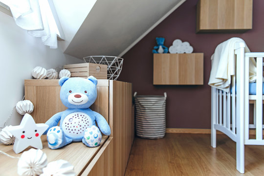 Stylish and cute scandinavian newborn baby room with toys, cotton lamps, teddy bears, baby cot and star. Modern interior with color background wall. Bright and sunny interior .