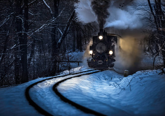 Budapest, Hungary - Beautiful winter forest scene with snow and old steam locomotive on the track in the Hungarian woods of Huvosvolgy at night © zgphotography