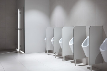 Row of clean porcelain sensor-operated male urinals with partitions in airport terminal. Light...