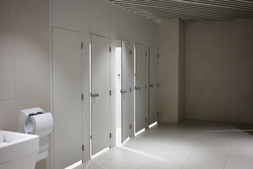 Public toilet cubicles in airport with white doors separated into male and female facilities,...