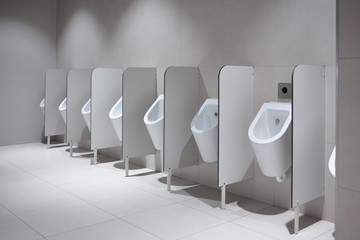 Line of white clean porcelain urinals in airport, cafe or restaurant. Public restroom for male users, minimalistic design. Typical arrangement of sensor-operated urinals in a row with partitions