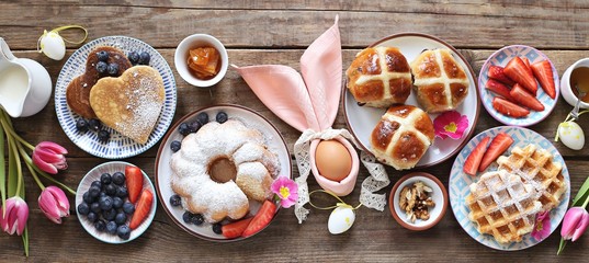 Easter festive dessert table with hot cross buns, cakes, waffles and pancakes. Overhead view