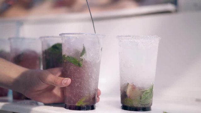 CU, 4k shot: Barman in the summer on the beach prepares fresh cocktails, with ice, mojito, fruits and berries. Shaking.