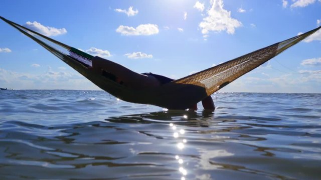 Happy young woman on vacation laying and resting in hammock at sunset in hot summer on Mexico beach