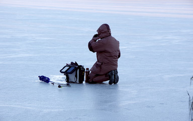 A lone fisherman sits on a frozen pond covered with snow and drinks coffee.