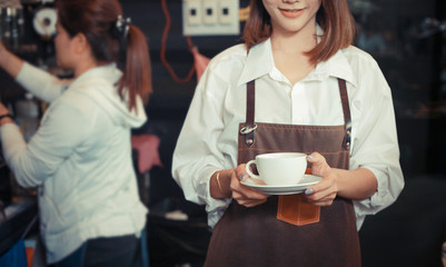 Young female barista serving coffee to customer in cafe.