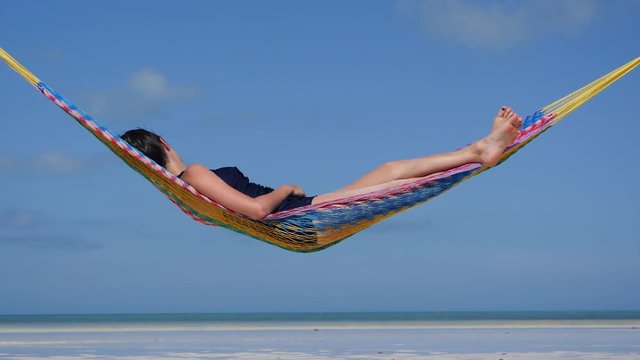 Happy young woman on vacation laying and resting in hammock at sunset in hot summer on Mexico beach