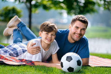 Father and son, lying together on a picnic blanket with ball, outdoors