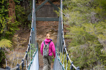 A female hiker crosses a swing bridge in the Abel Tasman, National Park, Nelson, New Zealand