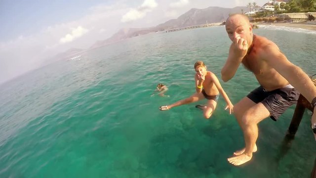 Father with a son jump into the blue sea from the bridge and makes selfie video.   Happy people's diving into the water from the wooden bridge . Slow motion. Mediterranean sea. Turkey. 