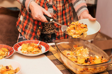 A woman at home cooked a delicious dinner - a baked potatoes with vegetables and sausages, and a woman puts food on plates for the whole family