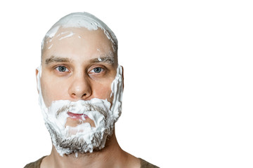 A guy with a beard with foam and gel on his face is preparing to shave in the morning at home on a colored background.