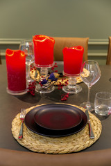 Christmas, holidays and table setting concept - glasses, dishes and red candles for a festive dinner at home