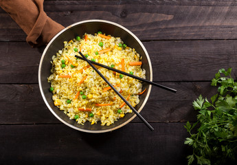 Cooked rice with curry and vegetables in a pan with chopsticks on the wood black background.