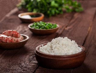 Cooked white rice in wooden bowl with shrimps, peas on the wood brown background.