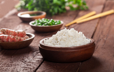 Cooked white rice in wooden bowl with shrimps, peas and chopsticks on the wood brown background.
