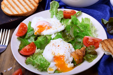 Poached egg with liquid yolk and green salad on a white plate